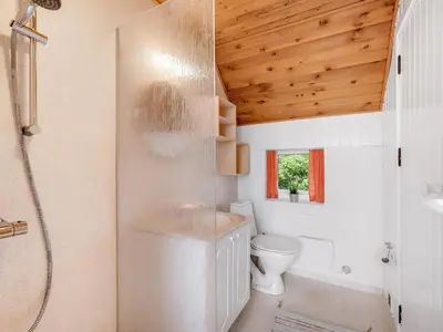 a bathroom with a toilet and a shower with a wooden ceiling at Holiday Home Balthasar - 200m from the sea by Interhome in Harboør