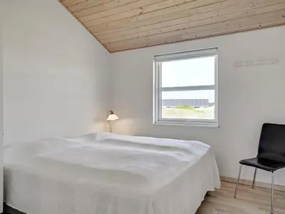 a white bedroom with a bed and a black chair at Holiday Home Frido - 400m from the sea by Interhome in Torsted