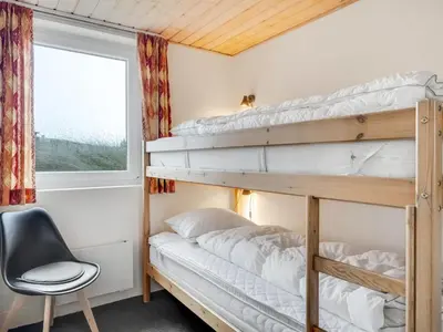 a bedroom with bunk beds with a chair and a window at Holiday Home Palli - 600m from the sea by Interhome in Torsted