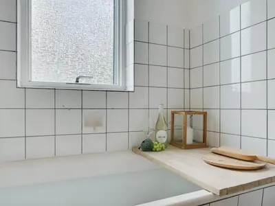 a white tiled bathroom with a tub and a window at Holiday Home Flor - 900m from the sea by Interhome in Torsted