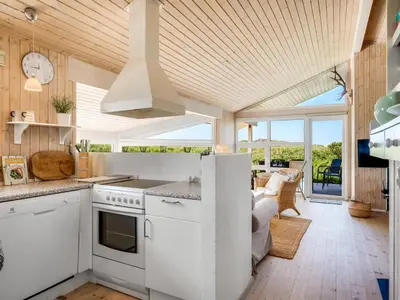 a kitchen with white cabinets and a view of a living room at Holiday Home Abel - 350m from the sea by Interhome in Løkken