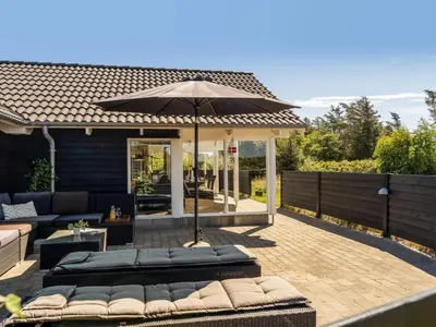 a patio with an umbrella and some couches and chairs at Holiday Home Federica - 500m from the sea by Interhome in Løkken