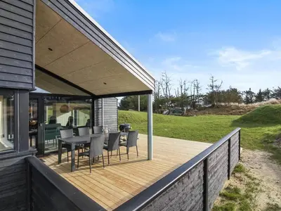 a deck with a table and chairs on a house at Holiday Home Vanamo - 300m from the sea by Interhome in Løkken