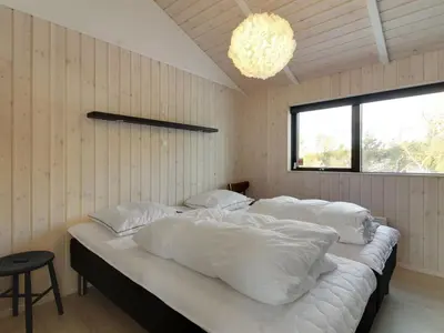 a bedroom with four beds with white sheets and a chandelier at Holiday Home Vanamo - 300m from the sea by Interhome in Løkken