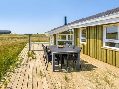 a wooden deck with a table and chairs in front of a house at Holiday Home Katla - 400m from the sea by Interhome in Løkken