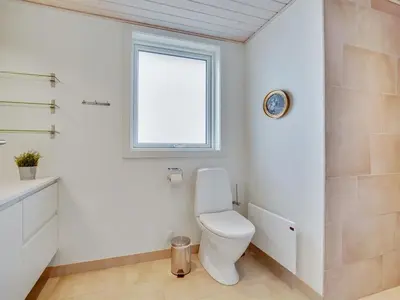 a white bathroom with a toilet and a window at Holiday Home Marthine - 200m from the sea by Interhome in Løkken