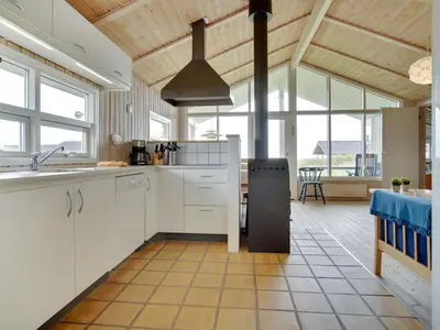 a kitchen with white cabinets and a table and windows at Holiday Home Viktoria - 400m from the sea by Interhome in Løkken