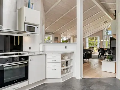 a kitchen with white cabinets and a living room at Holiday Home Dimo - 700m from the sea by Interhome in Løkken