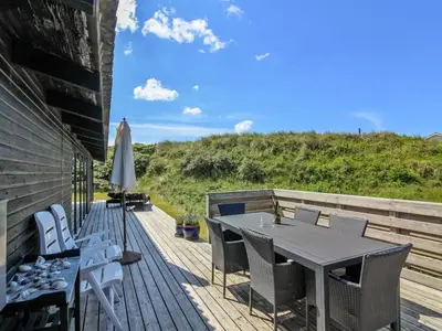 a wooden deck with a table and chairs and an umbrella at Holiday Home Tulir - 300m from the sea by Interhome in Løkken