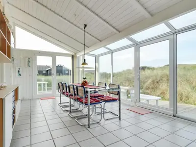 a dining room with a table and chairs and windows at Holiday Home Avni - 200m from the sea by Interhome in Løkken