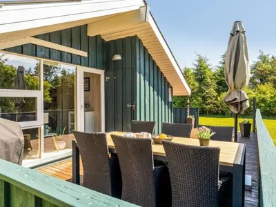 a wooden table with chairs and an umbrella on a deck at Holiday Home Seda - 600m from the sea by Interhome in Løkken