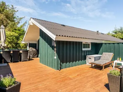 a green shed with a wooden deck with a grill at Holiday Home Seda - 600m from the sea by Interhome in Løkken