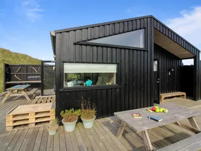 a black house with a wooden deck with a picnic table at Holiday Home Mikkel - 300m from the sea by Interhome in Løkken