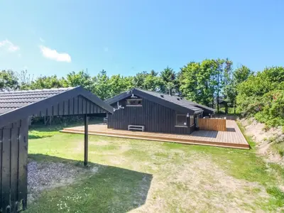 a black house with a wooden deck in a yard at Holiday Home Paulette - 450m from the sea by Interhome in Løkken