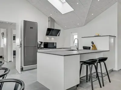 a white kitchen with a counter and stools at Holiday Home Fegge - 1-5km from the sea by Interhome in Løkken