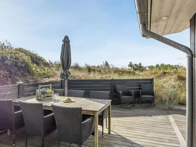 a wooden deck with a table and chairs and an umbrella at Holiday Home Elna - 400m from the sea by Interhome in Løkken
