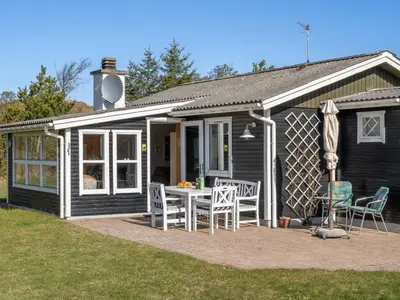 a black house with a table and chairs on a patio at Holiday Home Ingebritt - 1-5km from the sea by Interhome in Blokhus