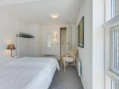 a white bedroom with a bed and a chair at Holiday Home Ninna - 1km from the sea by Interhome in Blokhus