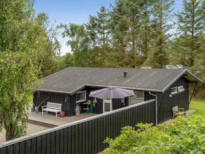 a black building with a deck and an umbrella at Holiday Home Bernadeta - 1-2km from the sea by Interhome in Blokhus
