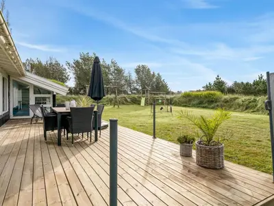 a wooden deck with a table and chairs and an umbrella at Holiday Home Helene - 1-5km from the sea by Interhome in Blokhus