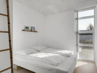 a bed in a white room with a window at Holiday Home Ilsabe - 2km from the sea by Interhome in Blokhus