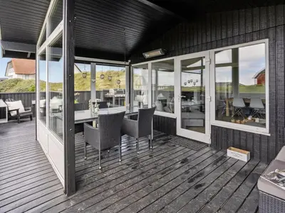 a deck with chairs and tables on a house at Holiday Home Kiina - 100m from the sea by Interhome in Blokhus