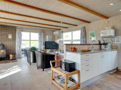 a kitchen with white cabinets and a living room at Holiday Home Dana - 290m from the sea by Interhome in Saltum