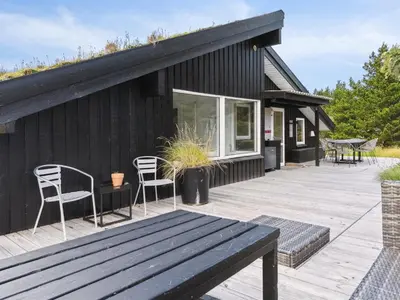 a black house with two chairs and a wooden deck at Holiday Home Nilson - 1-4km from the sea by Interhome in Blokhus