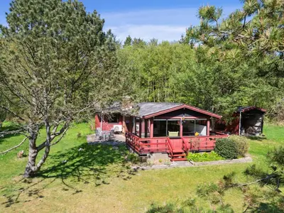 a red cabin in the middle of a field with trees at Holiday Home Therbern - 1-7km from the sea by Interhome in Saltum