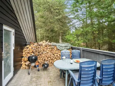 a patio with a table and chairs and a pile of wood at Holiday Home Varpu - 1-6km from the sea by Interhome in Saltum