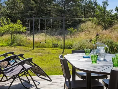 a wooden table and chairs on a deck with a swing at Holiday Home Swen - 1-3km from the sea by Interhome in Saltum