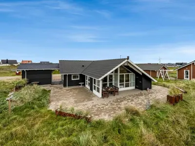 a black and white house in the middle of a field at Holiday Home Sochyeta - 150m from the sea by Interhome in Harboør