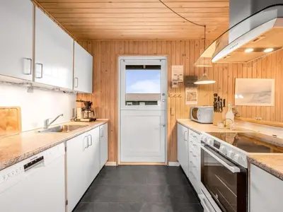 a kitchen with wooden walls and white cabinets at Holiday Home Odmar - 300m from the sea by Interhome in Harboør