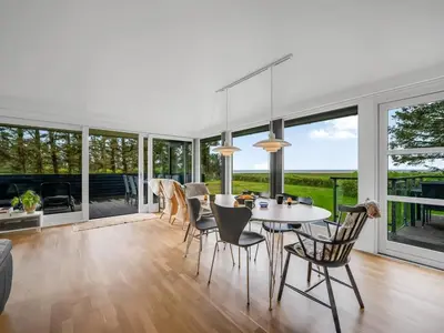 a dining room with a table and chairs and large windows at Holiday Home Aleida - 100m to the fjord by Interhome in Vemb