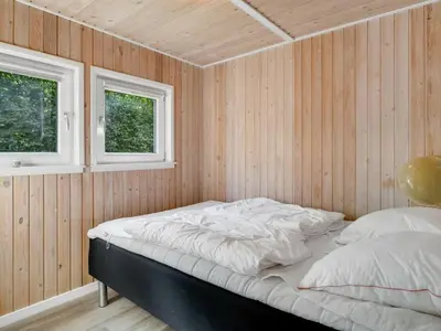a bed in a room with wooden walls and two windows at Holiday Home Eisa - 300m to the fjord by Interhome in Øsløs