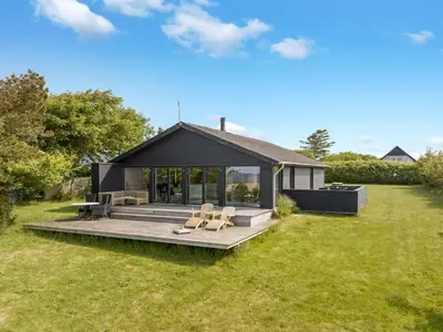 a black house with a deck in the grass at Holiday Home Aslag - 150m to the fjord by Interhome in Vinderup
