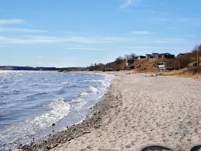 a sandy beach with houses on a hill next to the water at Holiday Home Aliza - 300m to the fjord by Interhome in Roslev