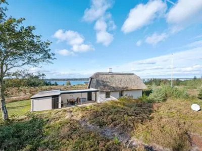 a small white house with a thatched roof on a field at Holiday Home Tordis - 250m to the fjord by Interhome in Roslev