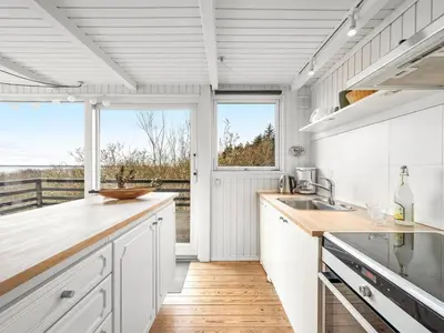 a kitchen with white cabinets and a large window at Holiday Home Heera - 100m to the fjord by Interhome in Lihme