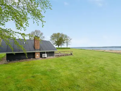 a house on a grassy field next to the water at Holiday Home Henrieke - 250m to the fjord by Interhome in Roslev