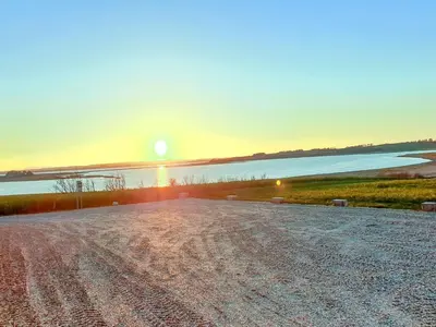 a sunset over a dirt road next to a body of water at Holiday Home Imilie - 250m to the fjord by Interhome in Redsted
