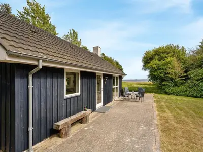 a black house with a bench and a table at Holiday Home Ødger - 150m to the fjord by Interhome in Åbybro