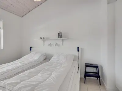 a white bedroom with a bed and a stool at Holiday Home Asel - 4km from the sea by Interhome in Brovst