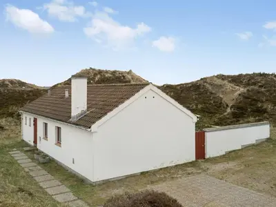 a white building in a field with mountains in the background at Holiday Home Emiljan - 400m from the sea by Interhome in Pandrup
