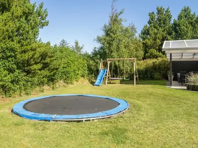 a trampoline and a playground in a yard at Holiday Home Wilja - 400m from the sea by Interhome in Fjerritslev
