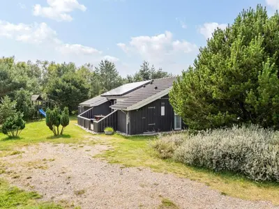 a black building in a field next to trees at Holiday Home Gothfred - 1km from the sea by Interhome in Fjerritslev