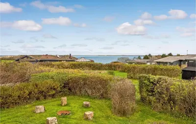 a field with rocks in the grass with houses and the water at Cozy Home In Hurup Thy With Wifi in Doverodde