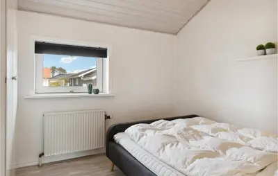 an unmade bed in a white room with a window at Nice Home In Blokhus With Sauna in Blokhus