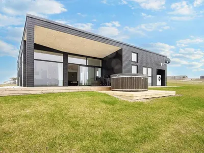 a black house with a large window on a field at 12 person holiday home in Lemvig-By Traum in Lemvig
