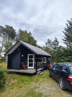 a black tiny house with a car parked in front of it at Tranum Klit Camping og Hytteudlejning in Brovst
